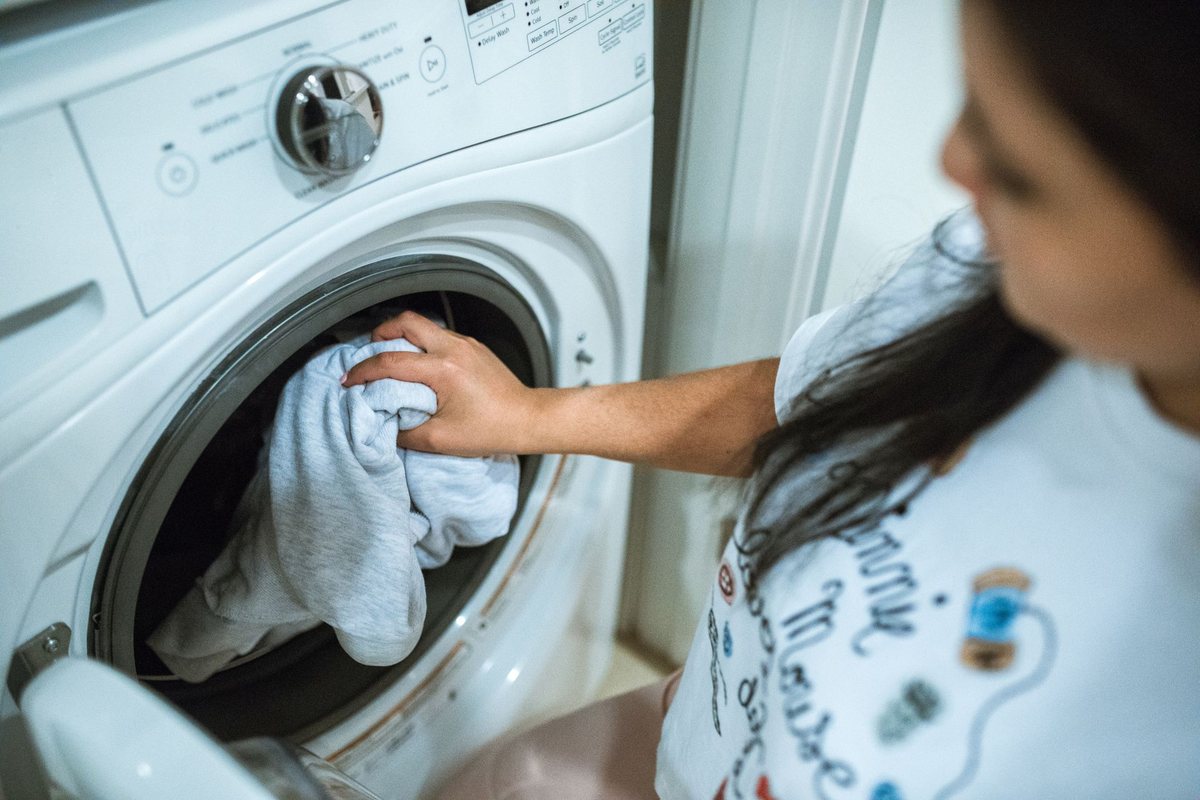 A woman loading laundry into a front-load washing machine at home, with no products or branding visible.