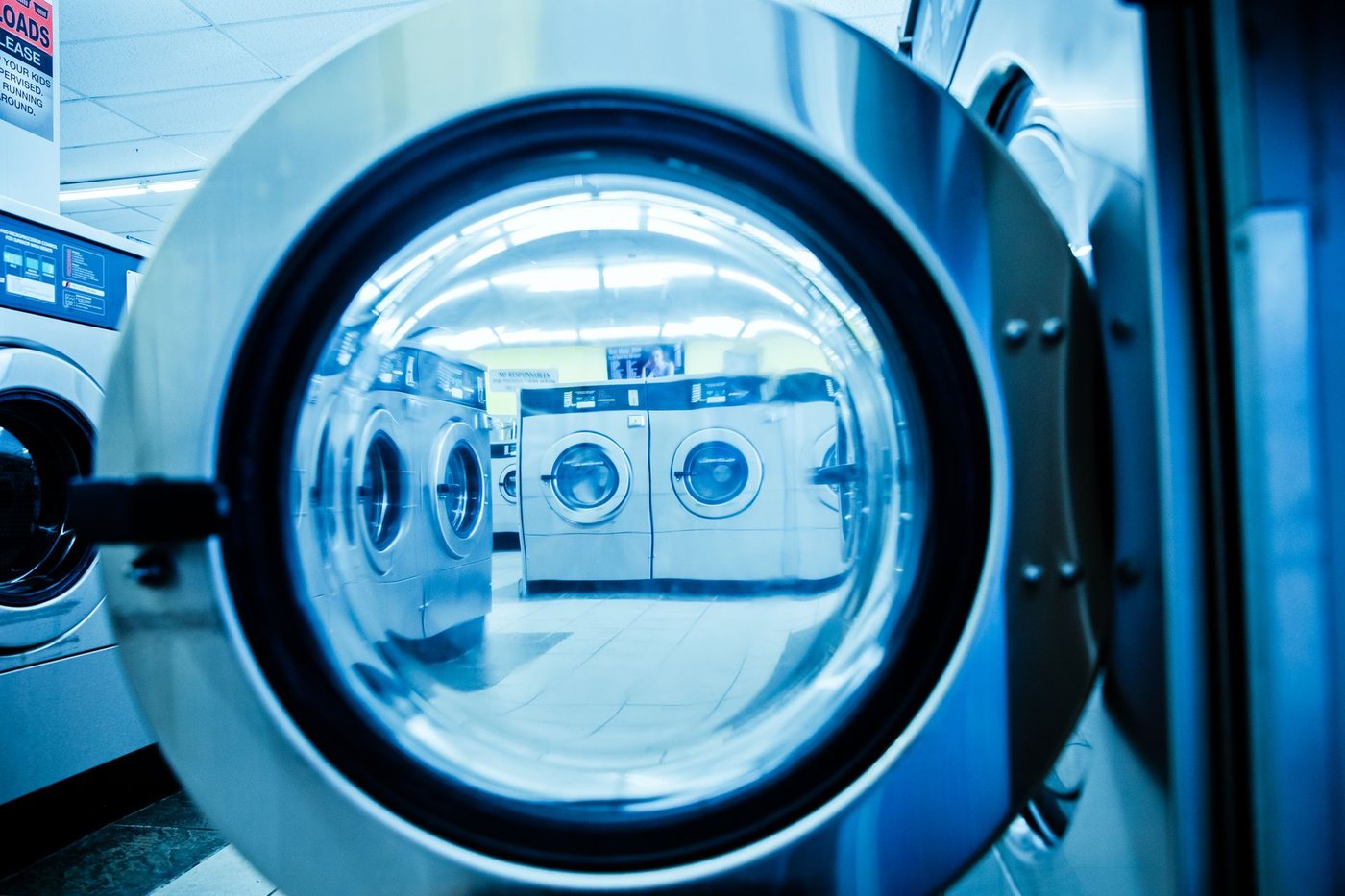 Rows of steel front-load washing machines in a modern laundromat, with no products or branding visible.