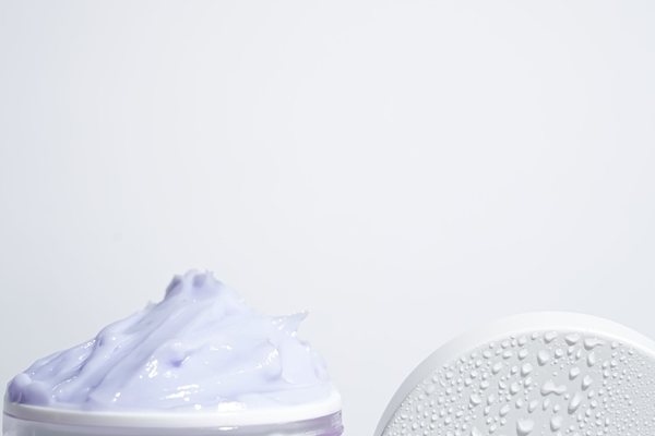Close-up of an open jar of purple azulene cream with water droplets on the lid.