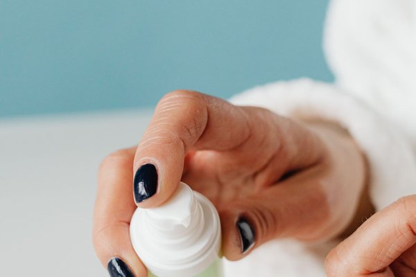 Close-up of a woman applying cream from a pump bottle.