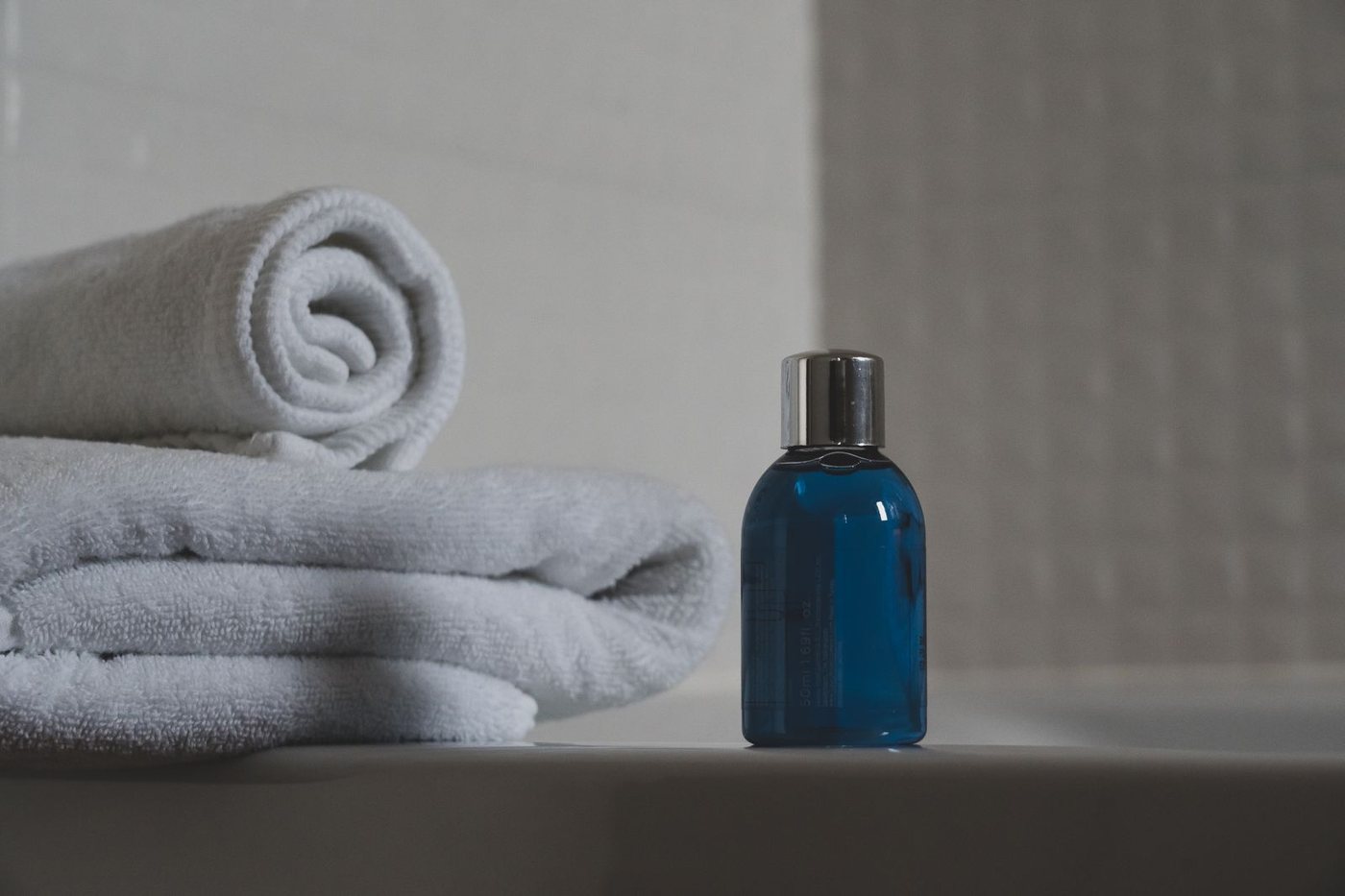An unlabelled blue bottle beside folded white towels, the kind of plain rinse-off product MI is used to preserve.