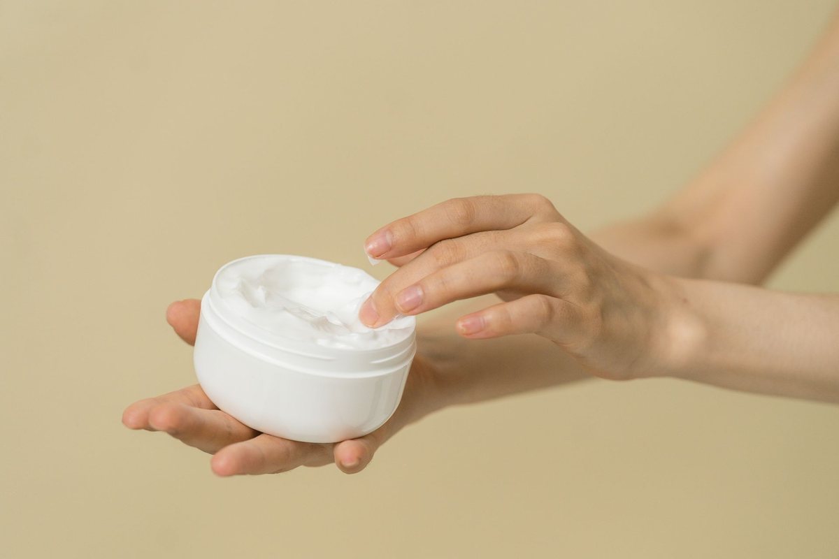 Close-up of hands taking moisturiser from an open jar, the everyday leave-on use phenoxyethanol preserves.